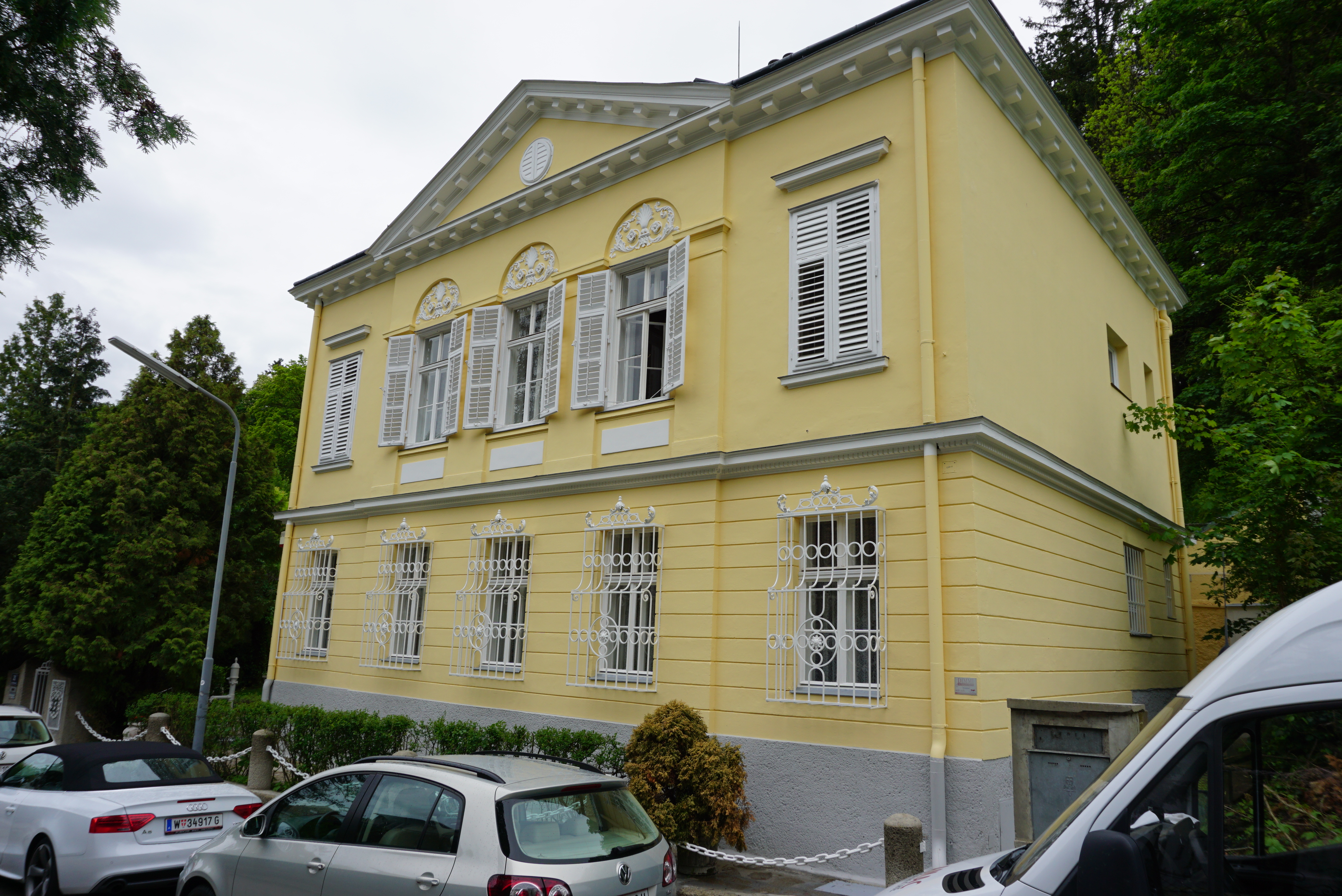 Exterior view of a two-storey townhouse painted pale yellow with white windows and shutters