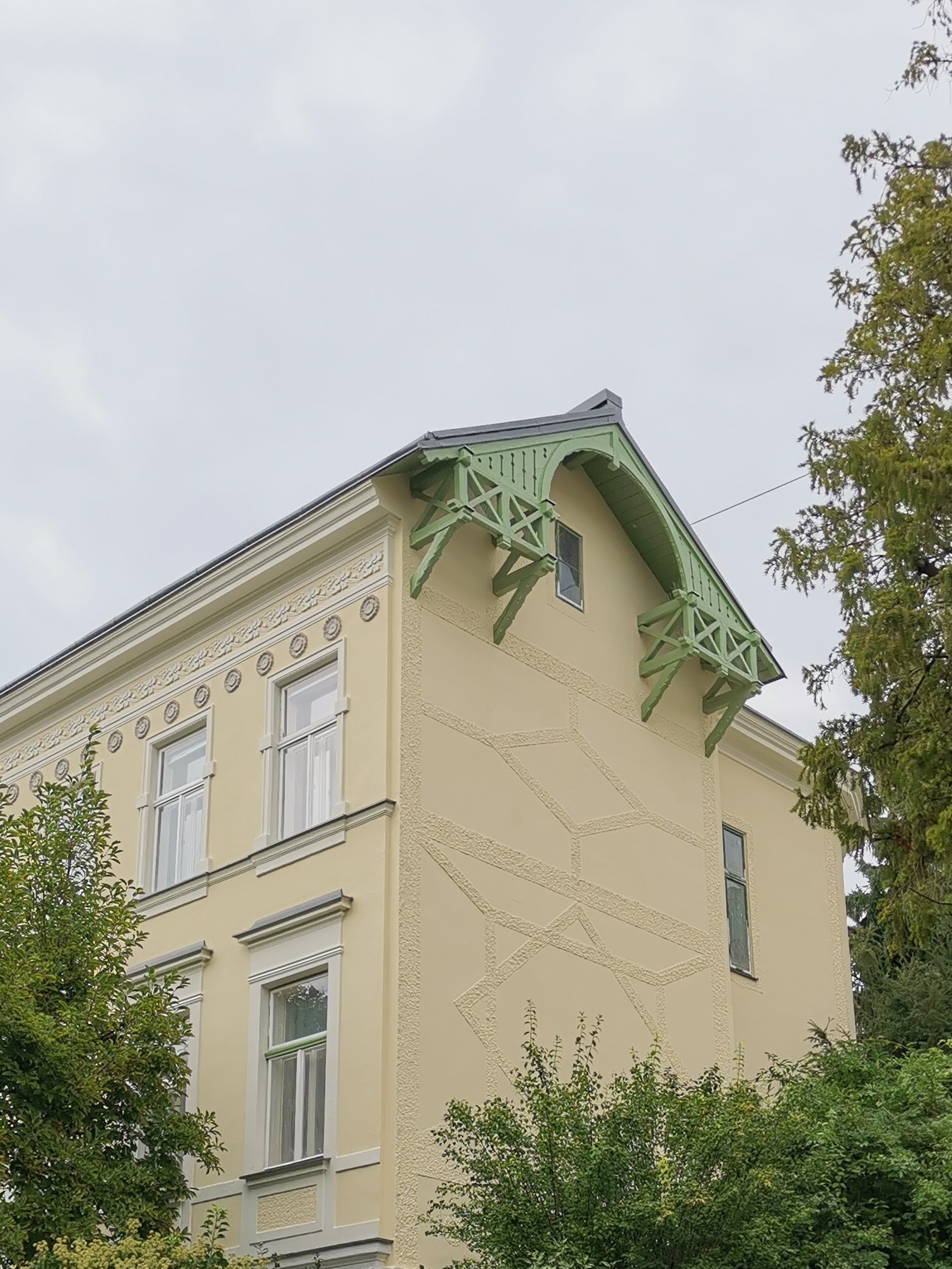 Partial view of a yellow painted house exterior with decorative wooden eaves painted pale green
